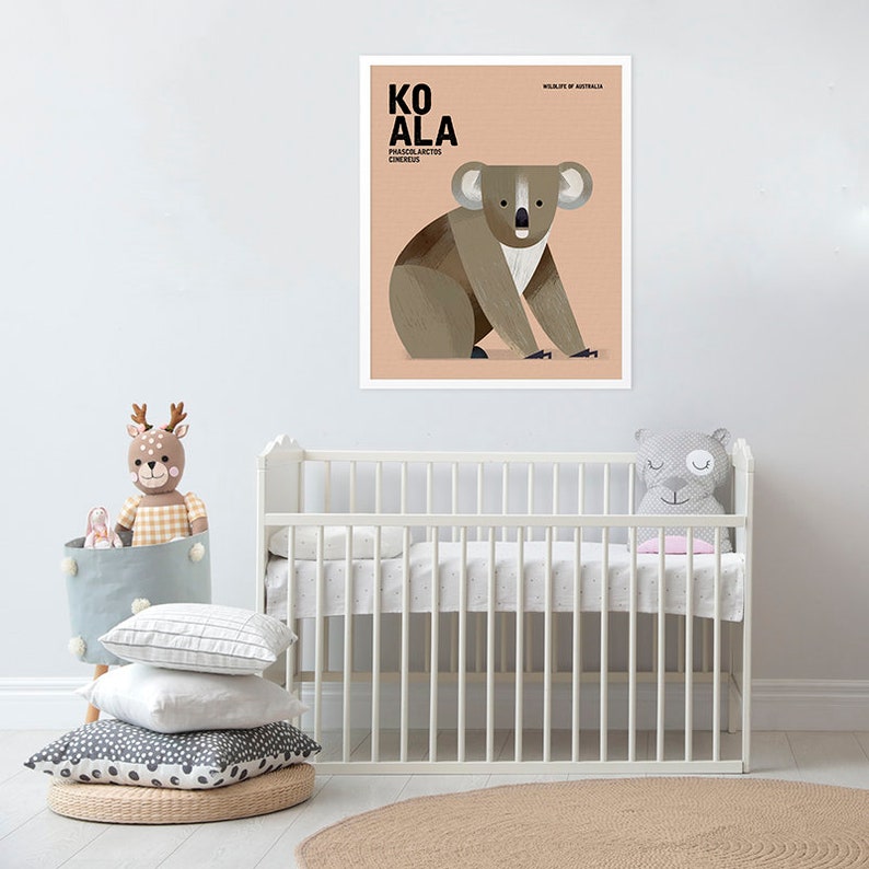 K&ouml;nnte beinhalten: Gerahmtes Poster mit einer Koala-Illustration in Braun-, Grau- und Wei&szlig;t&ouml;nen. Das Poster zeigt das Wort "KOALA" in Schwarz, den wissenschaftlichen Namen und "WILDLIFE OF AUSTRALIA". Das Poster h&auml;ngt &uuml;ber einem wei&szlig;en Babybett. Der Raum hat ein Babybett, Spielzeug und Kissen.