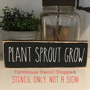 May include: Black wooden sign with white text that reads "PLANT SPROUT GROW". The sign has a white border and the text "Farmhouse Stencil Shoppe® STENCIL ONLY. NOT A SIGN!" is printed in red below the main text.