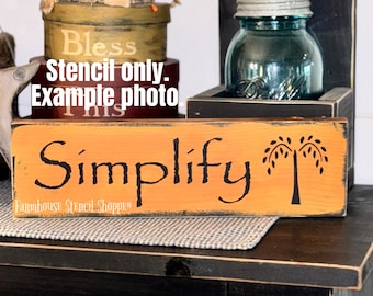 May include: Orange wooden sign with black lettering that reads "Simplify" and a black silhouette of a weeping willow tree. The sign is distressed and has a rustic look.  Stencil only. Example photo.