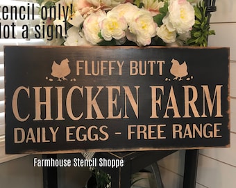 Puede incluir: Un letrero de madera negro con texto blanco que dice "FLUFFY BUTT CHICKEN FARM DAILY EGGS - FREE RANGE". El letrero también tiene dos siluetas blancas de pollos a cada lado del texto. El letrero está en un soporte de madera y hay flores en el fondo.