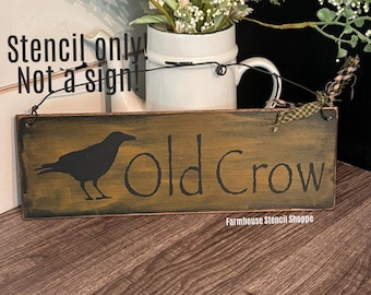 May include: A wooden sign with a distressed finish, featuring a black silhouette of a crow and the text "Old Crow". The sign is hanging from a wire and has a small piece of fabric tied to the top. The text "Farmhouse Stencil Shoppe" is printed at the bottom of the sign.
