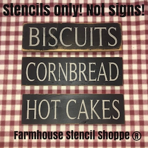 May include: Three black wooden signs with white lettering on a red and white checkered background. The signs read "Biscuits", "Cornbread", and "Hot Cakes". The text at the bottom of the image reads "Farmhouse Stencil Shoppe ®".