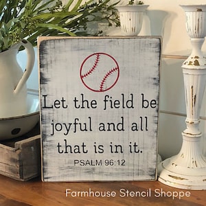 May include: White wooden sign with black text and a red baseball graphic. The text reads "Let the field be joyful and all that is in it. Psalm 96:12".