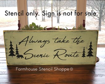 May include: A green wooden sign with white distressed paint and black lettering that reads "Always take the Scenic Route". The sign also features a black silhouette of two pine trees and a bear walking in front of the trees. The sign is on a wooden table and the text "Farmhouse Stencil ShoppeⓇ" is at the bottom of the sign.
