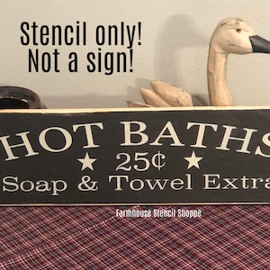 May include: Black wooden sign with white text that reads "HOT BATHS 25¢ Soap & Towel Extra" with two white stars. The sign is on a red and white checkered surface. The text "Stencil only! Not a sign!" is written in white on a gray background above the sign.