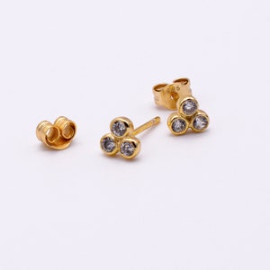 May include: A pair of gold earrings with three small clear stones in a triangular shape.