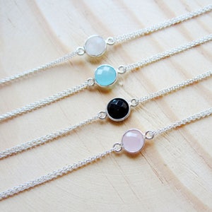 May include: Four delicate silver chain bracelets with a single gemstone charm on each. The charms are white, light blue, black, and pink.