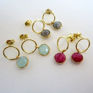 May include: Three pairs of gold hoop earrings with a dangling gemstone. The earrings feature a small gold hoop with a dangling gemstone in shades of blue, gray, and pink.