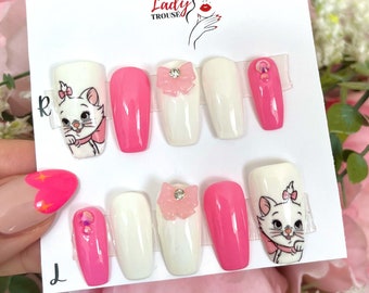 May include: Set of ten pink and white false nails with a cartoon cat design. The nails are long and have a coffin shape. The cat design is on two of the nails, and the other nails have a pink bow with a rhinestone.