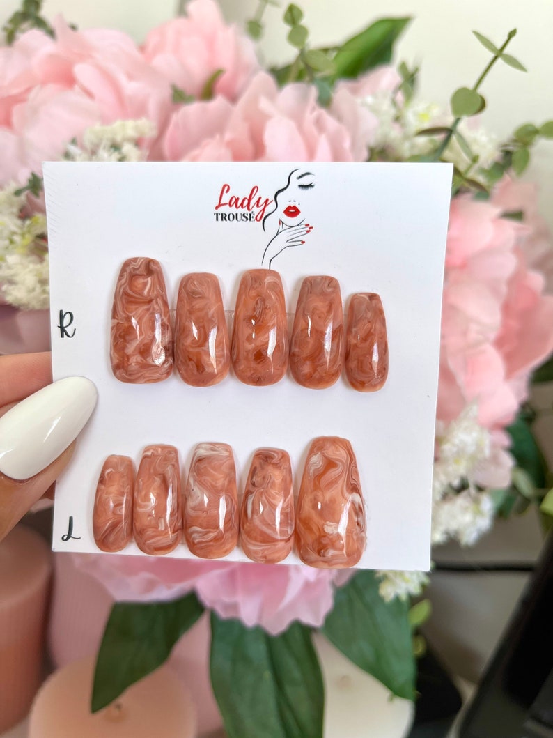 May include: Set of ten false nails with a brown and white marbled design. The nails are in a coffin shape and are arranged in two rows on a white card with the text "Lady Trousse" printed on it.
