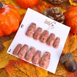 May include: Set of ten false nails with a brown and white marbled design. The nails are arranged in two rows on a white card with the text "Lady Trousse" printed on it.