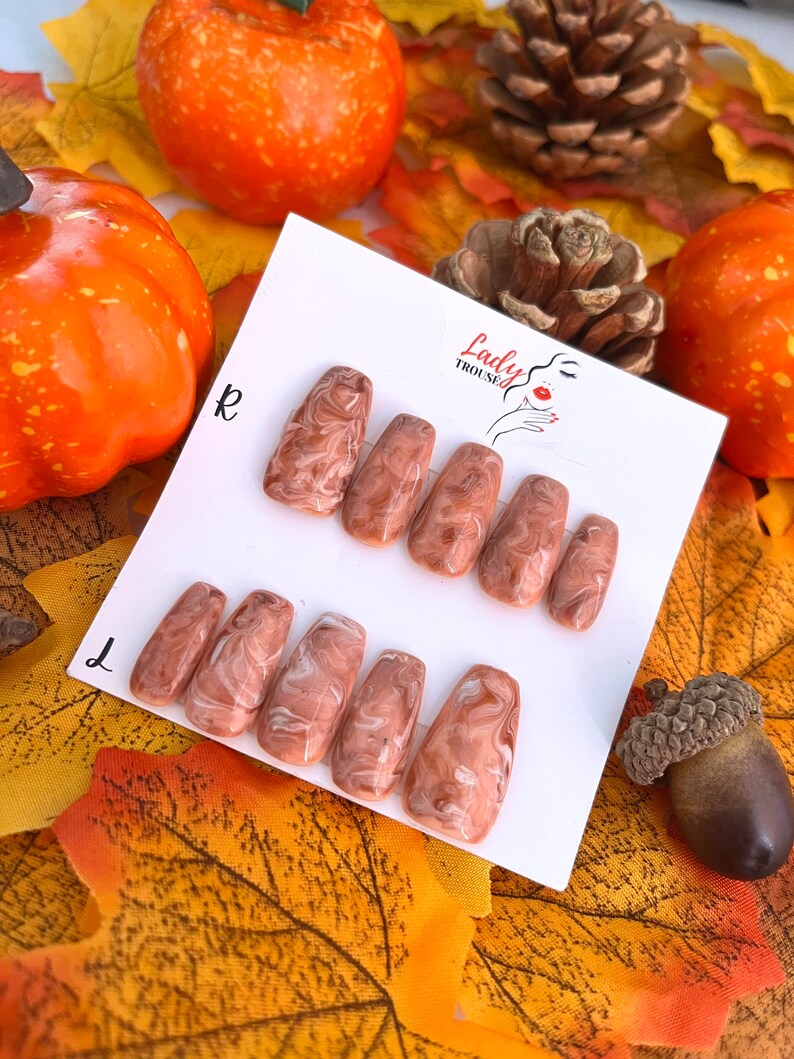 May include: Set of ten false nails with a brown and white marbled design. The nails are arranged in two rows on a white card with the text "Lady Trousse" printed on it.