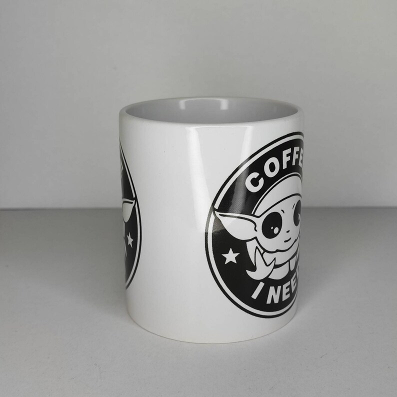 Pu&ograve; includere: Tazza in ceramica bianca con una grafica in bianco e nero di un personaggio dei cartoni animati con il testo "COFFEE I NEED" in un cerchio.