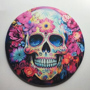 May include: A colorful sugar skull with blue eyes and a floral design. The skull is surrounded by pink, purple, and blue flowers.