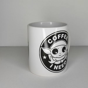 Pu&ograve; includere: Tazza da caff&egrave; in ceramica bianca con una grafica in bianco e nero di un personaggio dei cartoni animati con il testo "COFFEE I NEED" in un cerchio.