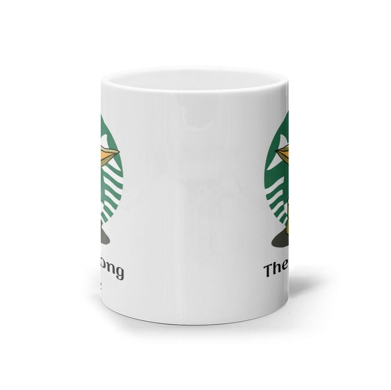 Puede incluir: Taza de cer&aacute;mica blanca con un c&iacute;rculo verde y una imagen de dibujos animados de un extraterrestre verde sosteniendo una taza. El texto "The Force" est&aacute; en el lado derecho de la taza y "Strong" est&aacute; en el lado izquierdo.
