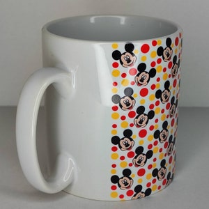 K&ouml;nnte beinhalten: Wei&szlig;e Keramiktasse mit einem roten und gelben Muster aus Mickey-Maus-Gesichtern.