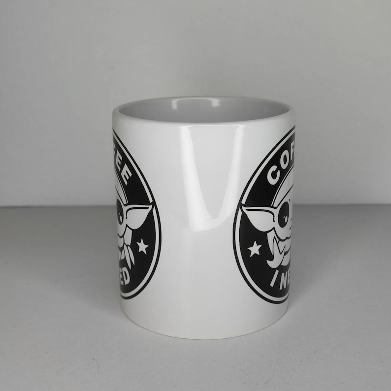 Pu&ograve; includere: Tazza da caff&egrave; in ceramica bianca con una grafica in bianco e nero di un personaggio dei cartoni animati con il testo "Coffee, I need it" in un cerchio.