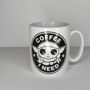 Pu&ograve; includere: Tazza da caff&egrave; in ceramica bianca con una grafica in bianco e nero di un personaggio dei cartoni animati con il testo "Ho bisogno di caff&egrave;" in un cerchio.