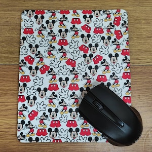 Puede incluir: Una alfombrilla de ratón blanca con un patrón repetido de cabezas de Mickey Mouse en rojo, negro y blanco. La alfombrilla de ratón está diseñada para ser utilizada con un ratón de ordenador.