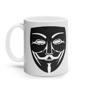 Puede incluir: Taza de cerámica blanca con una imagen en blanco y negro de la máscara de Anonymous. La máscara tiene una amplia sonrisa y una barba de chivo.