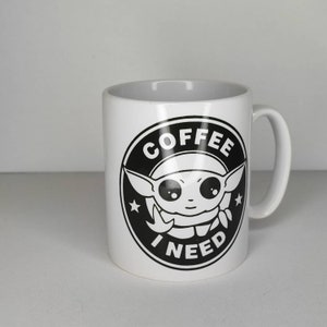 Pu&ograve; includere: Tazza da caff&egrave; in ceramica bianca con una grafica in bianco e nero di un personaggio dei cartoni animati con il testo "COFFEE I NEED" in un cerchio.