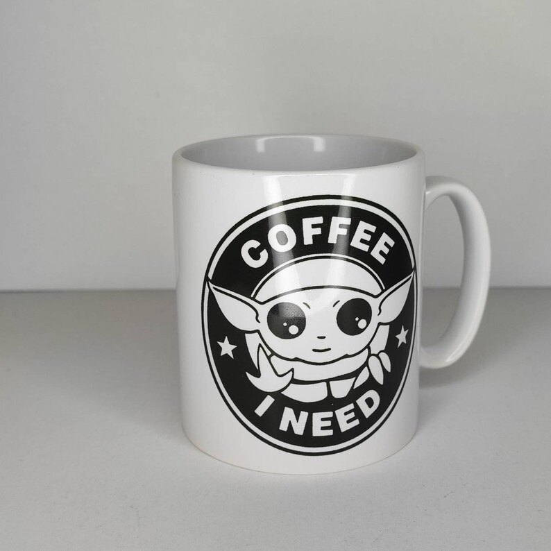 Pu&ograve; includere: Tazza da caff&egrave; in ceramica bianca con una grafica in bianco e nero di un personaggio dei cartoni animati con il testo "COFFEE I NEED" in un cerchio.