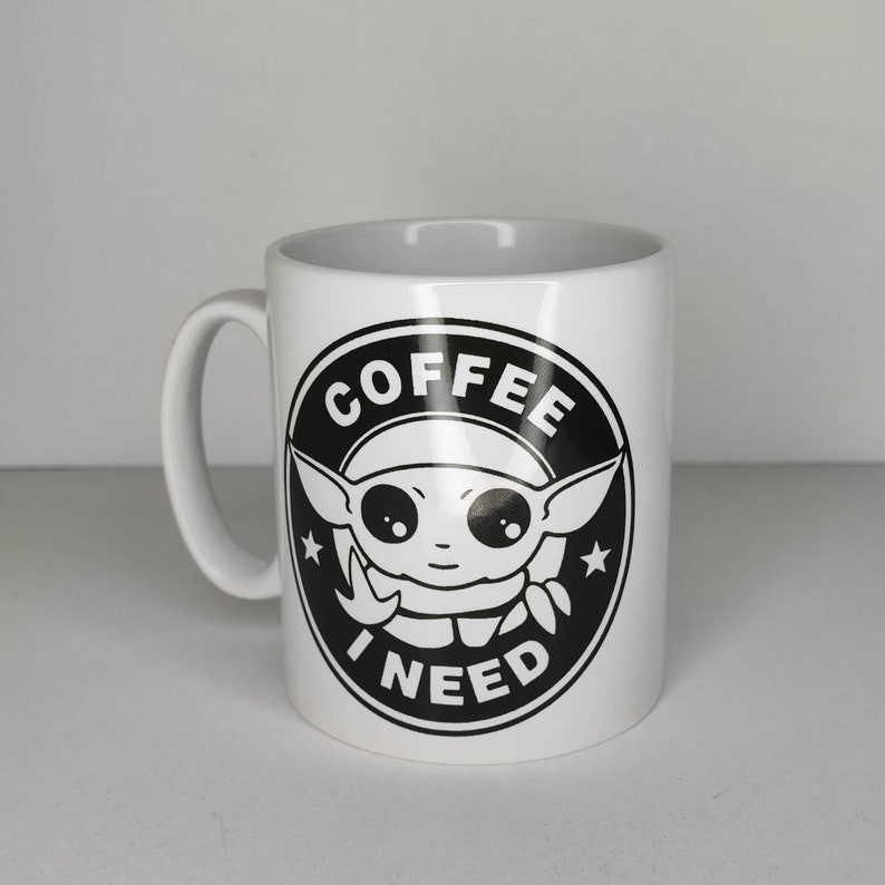 Pu&ograve; includere: Tazza in ceramica bianca con una grafica in bianco e nero di un personaggio dei cartoni animati con il testo "COFFEE I NEED" in un cerchio.