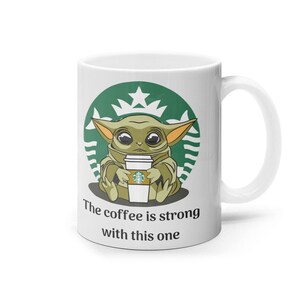 Puede incluir: Taza de cer&aacute;mica blanca con un logotipo de Starbucks verde y una imagen de dibujos animados de un extraterrestre verde sosteniendo una taza de caf&eacute; Starbucks. El texto "The coffee is strong with this one" est&aacute; impreso debajo de la imagen.