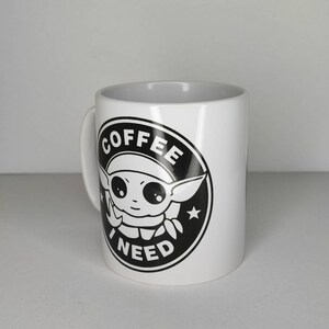 Pu&ograve; includere: Tazza da caff&egrave; in ceramica bianca con una grafica in bianco e nero di un personaggio dei cartoni animati con il testo "COFFEE I NEED" in un cerchio.