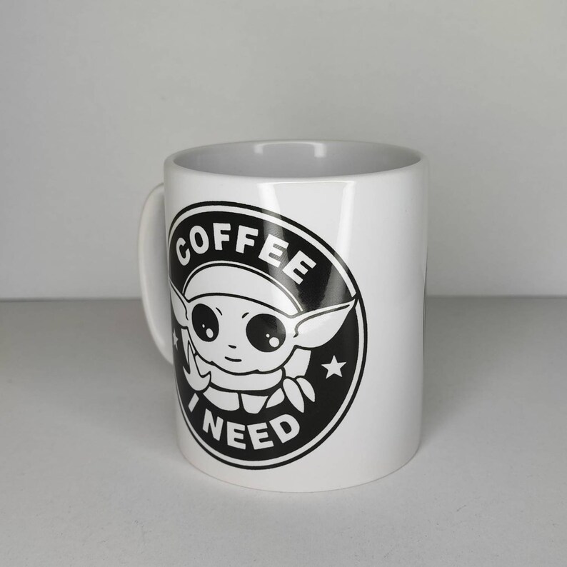 Pu&ograve; includere: Tazza da caff&egrave; in ceramica bianca con una grafica in bianco e nero di un personaggio dei cartoni animati con il testo "COFFEE I NEED" in un cerchio.