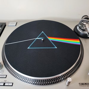 May include: A silver turntable with a black slipmat featuring the iconic "Dark Side of the Moon" album cover art. The album cover art features a prism refracting light into a rainbow, a white beam of light, and a triangle.
