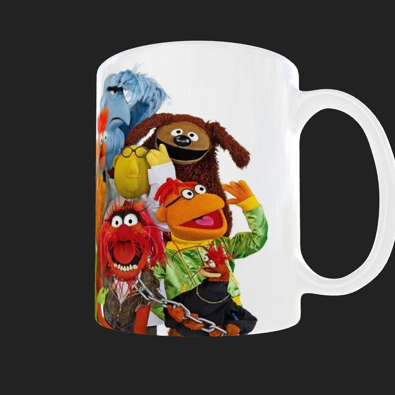 K&ouml;nnte beinhalten: Wei&szlig;e Keramiktasse mit einem bunten Bild von f&uuml;nf Muppet-Charakteren. Die Charaktere sind Animal, Dr. Bunsen Honeydew, Beaker, Cookie Monster und Grover.