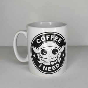 Pu&ograve; includere: Tazza in ceramica bianca con una grafica in bianco e nero di un personaggio dei cartoni animati con il testo "COFFEE I NEED" in un cerchio.