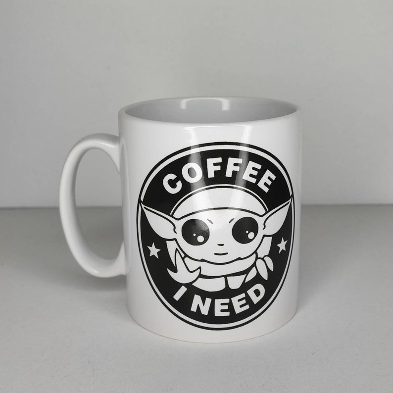 Pu&ograve; includere: Tazza in ceramica bianca con una grafica in bianco e nero di un personaggio dei cartoni animati con il testo "COFFEE I NEED" in un cerchio.