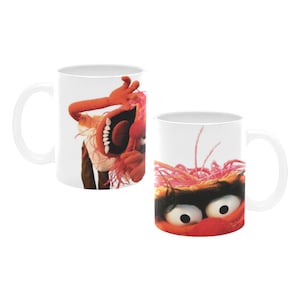 Könnte beinhalten: Zwei weiße Keramikbecher mit der Muppet-Figur Animal. Auf einem Becher ist Animal mit offenem Mund zu sehen, auf dem anderen sein Gesicht. Die Becher haben einen weißen Henkel und eine weiße Innenseite.