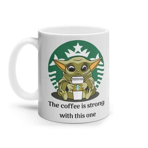 Puede incluir: Taza de cer&aacute;mica blanca con un logotipo de Starbucks verde y una imagen de dibujos animados de un extraterrestre verde sosteniendo una taza de caf&eacute; Starbucks. El texto "The coffee is strong with this one" est&aacute; impreso debajo de la imagen.