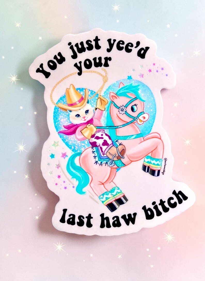 Op de afbeelding: Een gestanste sticker met een cartoonkat op een roze paard, beide gekleed in cowboykleding. De sticker heeft de tekst "You just yee'd your last haw bitch" in zwarte letters. De achtergrond is een pastelkleurige gradi&euml;nt.