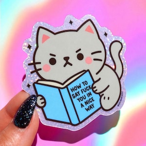 May include: A sticker featuring a gray cat reading a blue book with the text "HOW TO SAY FUCK YOU IN A NICE WAY." The cat has a grumpy expression and is surrounded by a glittery border.