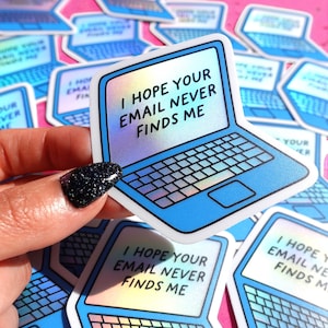 Może przedstawiać: Kolekcja naklejek w kształcie laptopa z niebieskim i holograficznym wzorem. Każda naklejka zawiera tekst "I HOPE YOUR EMAIL NEVER FINDS ME" na ekranie. Naklejki są trzymane przez dłoń z czarnym brokatowym paznokciem.