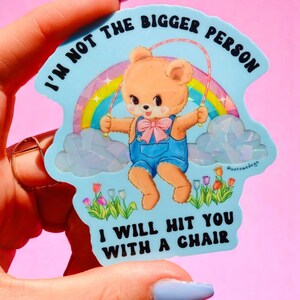 May include: A light blue sticker with a cartoon bear jumping rope in front of a rainbow. The sticker has the text "I'm not the bigger person, I will hit you with a chair."