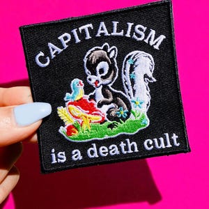 Puede incluir: Parche cuadrado negro con las palabras "CAPITALISM" y "is a death cult" en blanco. El parche presenta una mofeta de dibujos animados, un pájaro y flores sobre un campo verde. El fondo es rosa brillante.