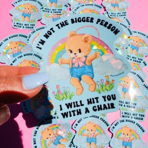 May include: A collection of light blue stickers featuring a cartoon teddy bear skipping rope in front of a rainbow. The text on the sticker says "I'M NOT THE BIGGER PERSON, I WILL HIT YOU WITH A CHAIR."