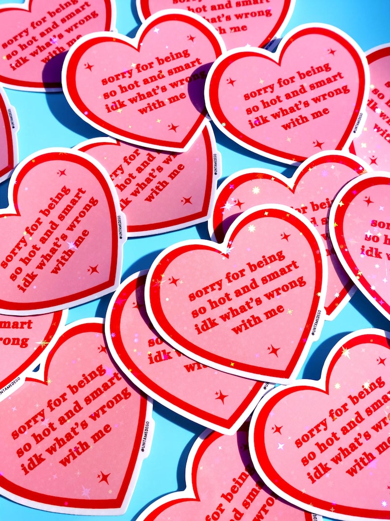 Pu&ograve; includere: Una collezione di adesivi rosa a forma di cuore con bordo rosso e la scritta "sorry for being so hot and smart idk what's wrong with me". Gli adesivi hanno un effetto glitterato e sono sparsi su una superficie azzurra.