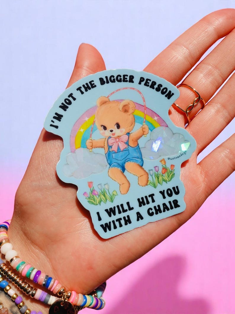 May include: A light blue sticker featuring a cartoon bear skipping rope in front of a rainbow. The text on the sticker reads "I'M NOT THE BIGGER PERSON I WILL HIT YOU WITH A CHAIR."