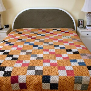 May include: A yellow, white, red, blue, and black patchwork quilt with a checkered pattern on a white bed frame with a brown headboard.