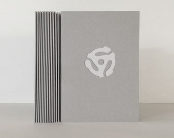 May include: A stack of gray cardstock paper with a white vinyl record symbol cut out on the front.