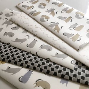 May include: Five different wrapping paper designs featuring cats in various poses. The designs include a black and white chequered pattern, a white background with grey and brown cats, and a white background with grey cats.
