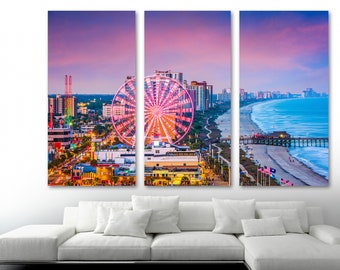 May include: A panoramic view of a coastal city at sunset with a Ferris wheel in the foreground. The city skyline is visible in the distance, with a beach and pier in the foreground. The sky is a vibrant pink and orange.