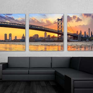 Peut inclure: Une vue panoramique du ciel de Philadelphie au coucher du soleil, mettant en vedette le pont Benjamin Franklin et les gratte-ciel emblématiques de la ville. Le pont est illuminé par le soleil couchant, projetant une lueur chaude sur le paysage urbain. L'eau sous le pont reflète la lumière dorée, créant une scène sereine et pittoresque.